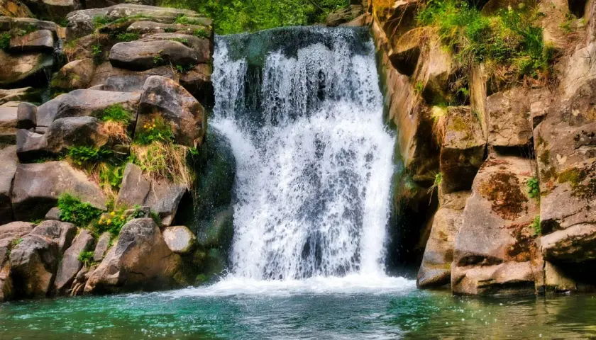Wodospad w skalistej scenerii, idealny cel dla miłośników **best waterfall hikes**. Zielona woda i bujna roślinność.