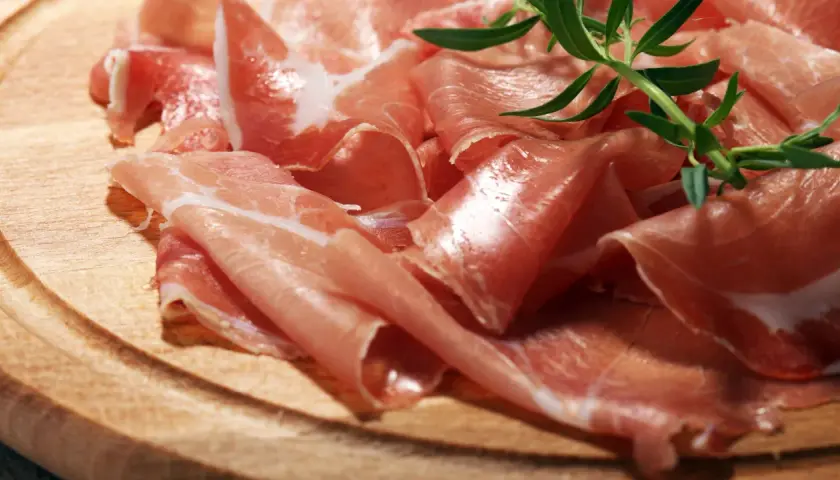 Cienkie plastry prosciutto crudo, ułożone na drewnianej desce, z gałązką rozmarynu. Pyszne, prawda?