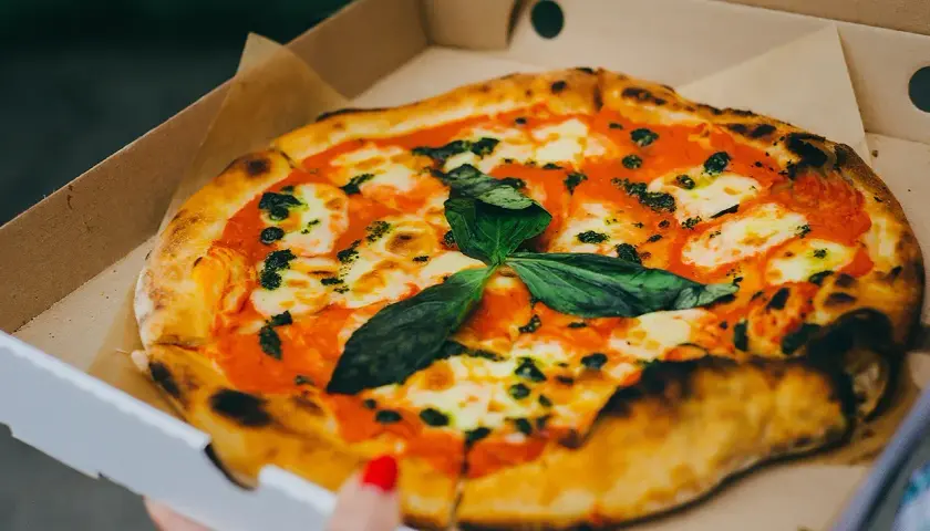 Pyszna pizza w kartonie na pizze, z sosem pomidorowym, mozzarellą i świeżą bazylią. Idealna na wynos!