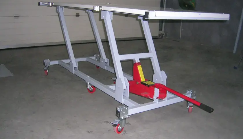 Elevador moto casero con gato hidráulico rojo, estructura metálica gris y ruedas. Ideal para reparaciones.