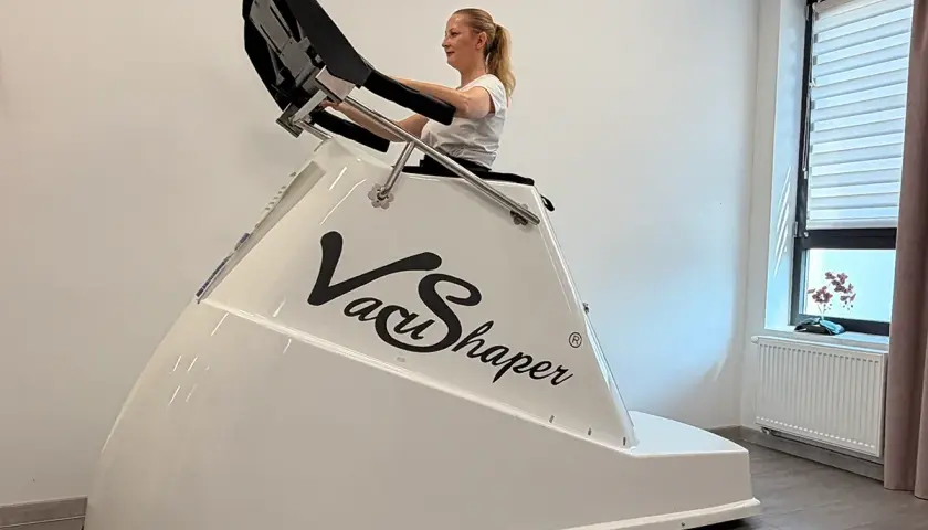 Kobieta ćwiczy na urządzeniu Vacu Shaper, które pomaga w modelowaniu sylwetki.