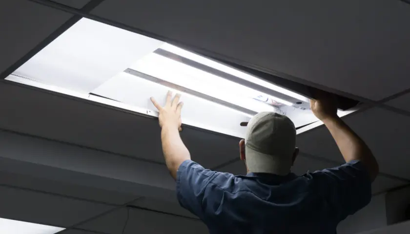 Pracownik w czapce wymienia świetlówki na led w suficie podwieszanym.