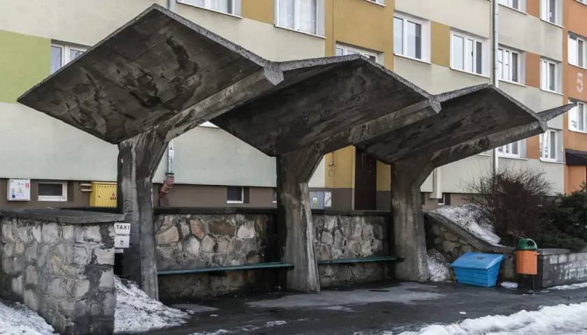 Surowa, betonowa wiata przystankowa, przykład brutalizmu w sztuce, z kamiennym murem i ławkami.