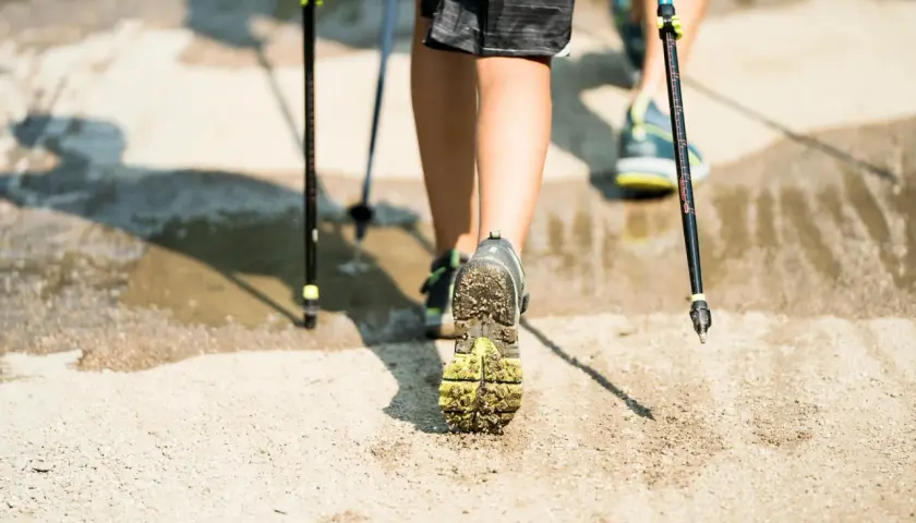 Nordic walking - jak chodzić, żeby schudnąć. Dwie osoby maszerują z kijkami po wilgotnym, piaszczystym podłożu.