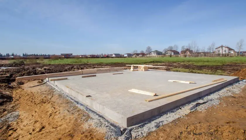Płyta fundamentowa domu w budowie, otoczona ziemią i drewnem.