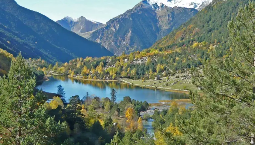 El estany de Llebreta, un lago alpino rodeado de bosques otoñales y montañas nevadas, ofrece una vista serena y colorida.