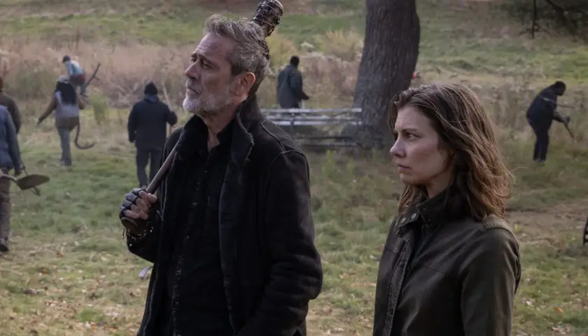 Maggie et Negan, le regard lointain, se tiennent côte à côte dans un paysage automnal. D'autres survivants travaillent en arrière-plan.