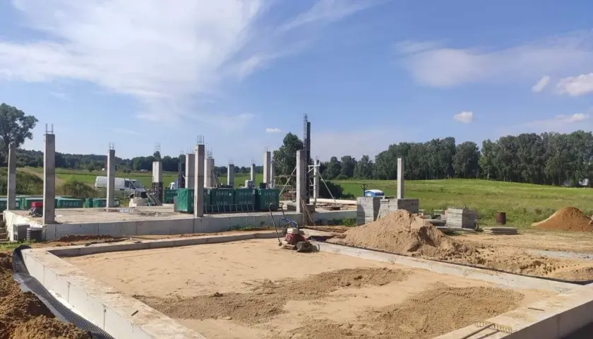 Budowa domu w toku. Widać fundamenty, słupy betonowe i sprzęt do wibrowania betonu.