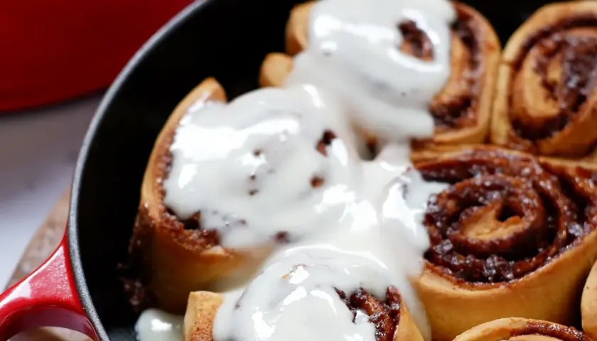 Deliciosos rollitos de canela recién horneados, cubiertos con un glaseado cremoso, listos para disfrutar.