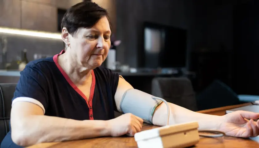 Kobieta w średnim wieku mierzy ciśnienie. Dba o prawidłowe ciśnienie tętnicze u 50-latka, monitorując je w domu.