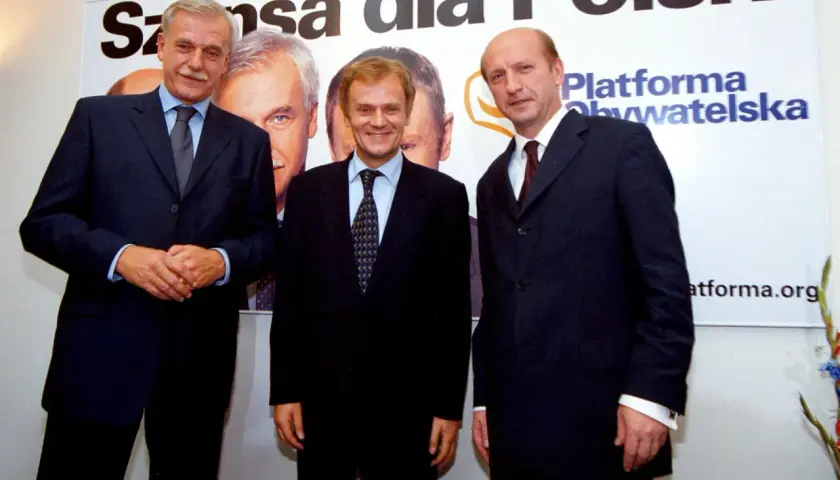 Trzech mężczyzn w garniturach, założyciele Platformy Obywatelskiej, pozuje na tle banera z napisem "Szansa dla Polski".