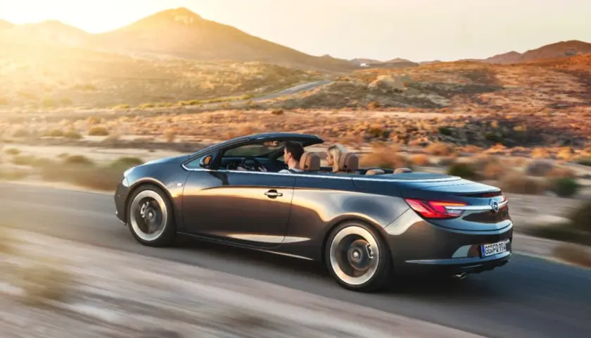 Para podróżuje kabrioletem Opel Cascada przez pustynny krajobraz o zachodzie słońca.