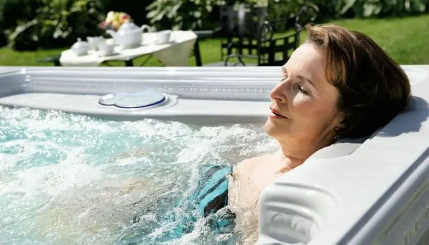 Une femme se détend dans un jacuzzi, profitant de l'eau chaude. Elle se demande combien de temps dans un jacuzzi est idéal pour se relaxer.