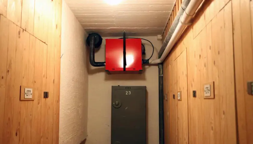 Röd radonfläkt monterad på väggen i en källarkorridor med träpaneler. En ventilationstrumma leder bort luften.