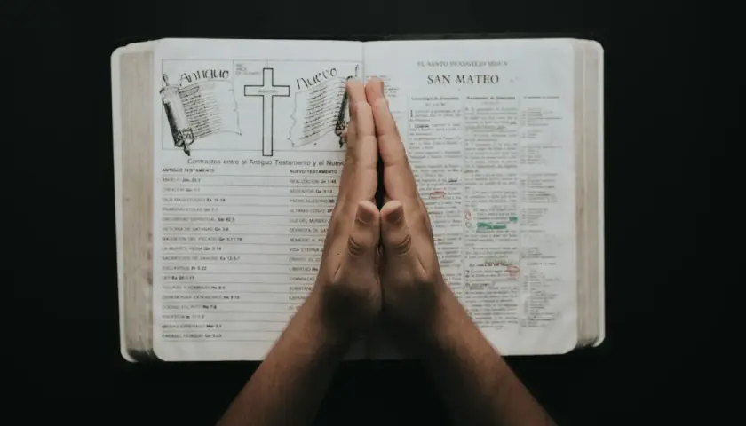 Dłonie złożone w modlitwie nad otwartą Biblią, w której widnieje porównanie Starego i Nowego Testamentu. To chwila refleksji i psalmy uwielbienia.