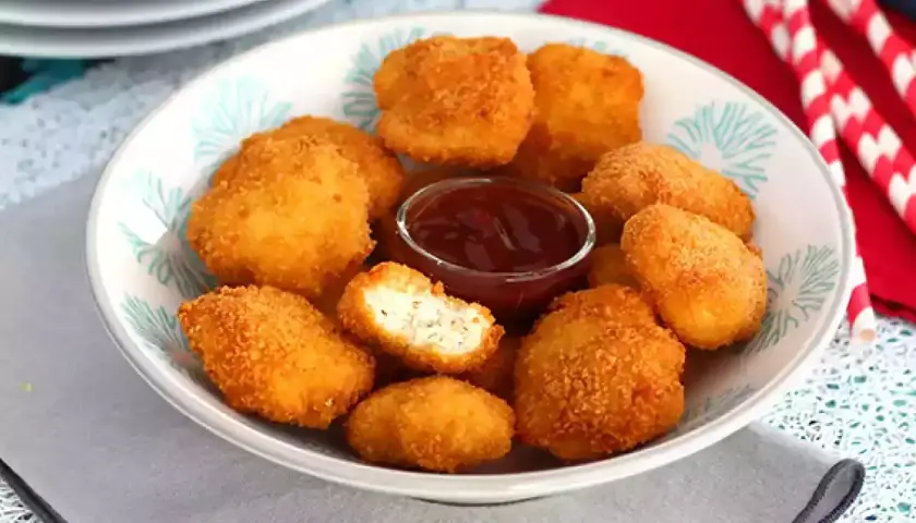 En skål med gyllene chicken nuggets och en liten skål med ketchup. Perfekt för en snabb och god måltid.