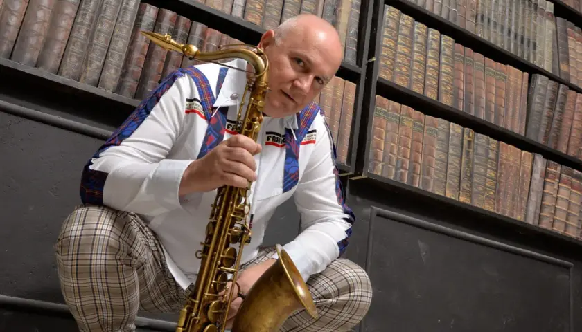 Mann mit Saxophon vor Bücherregal, bereit, einen Saxophon-VST-Sound zu erzeugen.