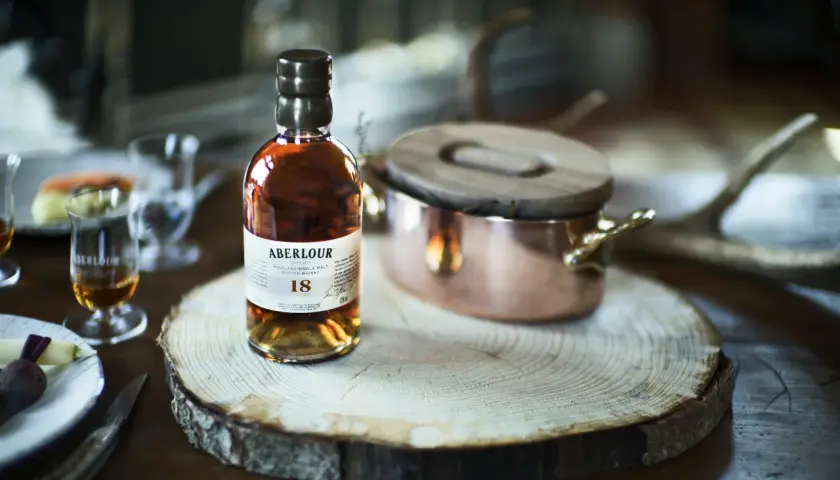 Bouteille d'Aberlour 18 ans, un whisky d'exception, posée sur une tranche de bois. Une expérience de dégustation unique, fruit d'une **création whisky** raffinée.
