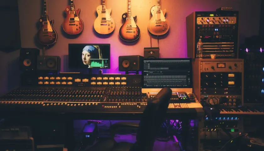 Guitars suspendus au-dessus d'une console de mixage, d'écrans et de racks d'équipement studio d'enregistrement, baignant dans une lumière violette.