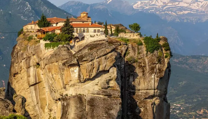 Monastery perched atop a massive rock formation in Meteora, Greece. The ancient stone buildings with red-tiled roofs seem to defy gravity, offering a glimpse into timeless Meteora hours.
