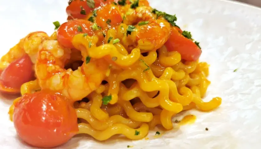 Un piatto invitante di pasta con gamberetti, pomodorini succosi e un tocco di prezzemolo fresco.