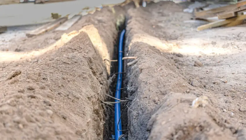 Wykopany rów z niebieską rurą, prawdopodobnie na jakiej głębokości kabel elektryczny zostanie ułożony.