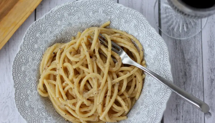 Pyszne cacio e pepe na talerzu z ozdobnym wzorem. Widok z góry na makaron z serem i pieprzem, obok widelec.