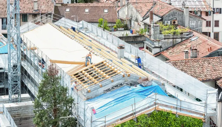 Pracownicy realizują projektowanie dachu, montując drewnianą konstrukcję na budynku.