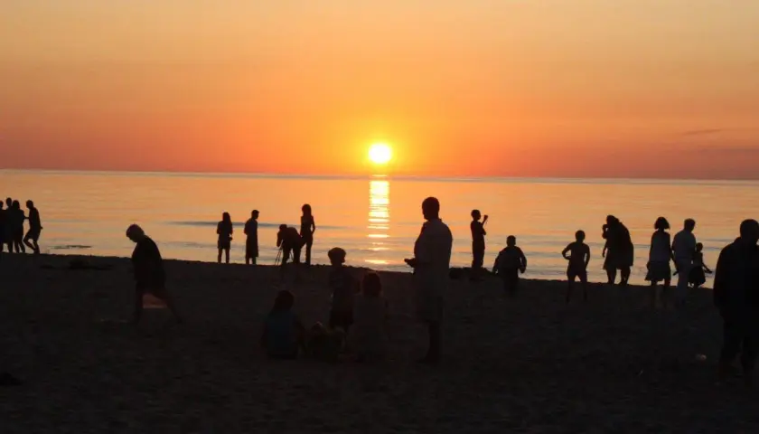 Sylwetki ludzi na plaży o zachodzie słońca nad morzem.