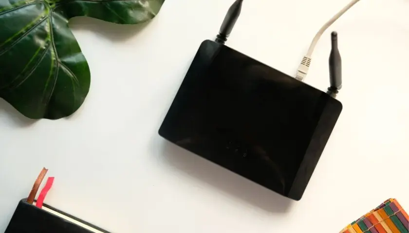 Czarny router z antenkami i kablem. Obok liść, notatnik i kolorowa podkładka. Czy router pobiera dużo prądu?