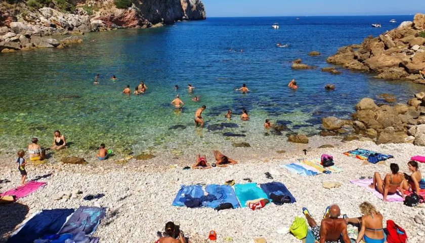 Plage de galets à Terrasini, Sicile. Des baigneurs profitent de l'eau cristalline sous un soleil radieux.