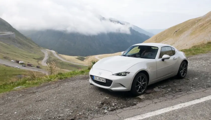 Un Mazda MX5 blanco en una carretera de montaña. Las opiniones sobre este coche son muy positivas, ideal para disfrutar de paisajes así.