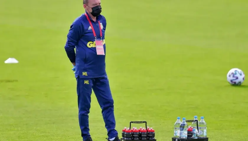 Mężczyzna w niebieskim dresie i masce na twarzy, z napisem "ML" na nogawce, stoi na boisku. To kitman, który dba o zawodników.