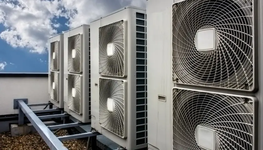 Rząd jednostek klimatyzacyjnych na dachu pod błękitnym niebem z chmurami.