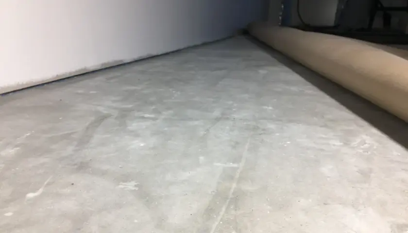 Ojämn betongyta som väntar på att slipa betong för en jämn finish. En rulle skyddspapper ligger längs väggen.