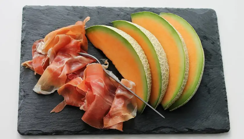 Tranche de melon et jambon cru sur ardoise. Quel vin avec melon et jambon cru ? Un vin blanc sec et fruité ou un rosé léger serait parfait.