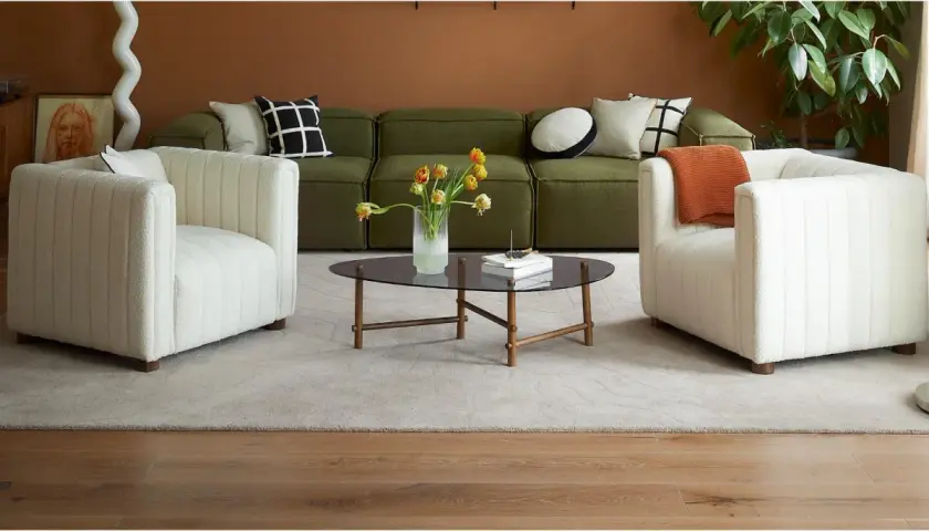 Ein grünes Sofa mit Kissen, die das Sofa dekorieren und richtig kombinieren. Zwei weiße Sessel und ein Couchtisch mit Blumen.