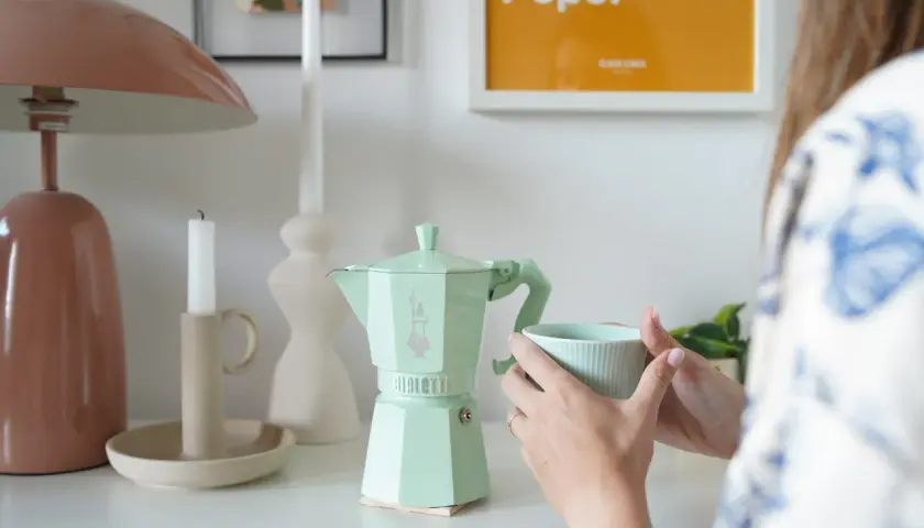 Miętowa kawiarka Bialetti, czy stalowa czy aluminiowa, idealna na poranną kawę. Obok świeca i kubek.