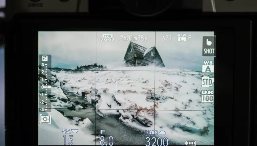 Ekran aparatu z widokiem na zasypany śniegiem dom. Poradnik fotograficzny podpowiada ustawienia: ISO 3200, f/8.0, czas 15s.