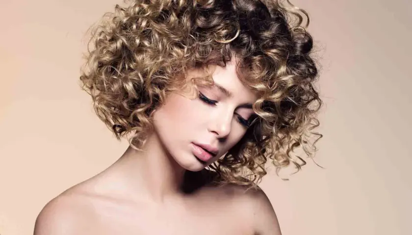Mujer con un moderno bob cortes de pelo rizado, con reflejos rubios y castaños, mirada serena.