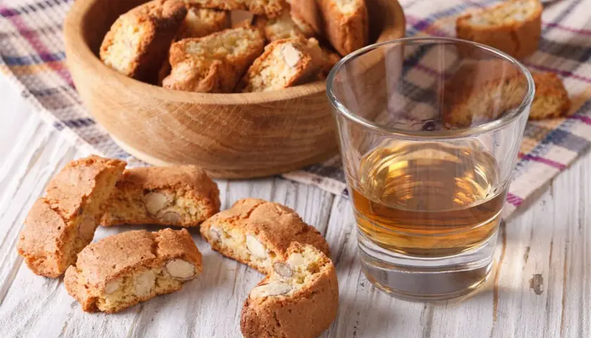 Kieliszek wina Vin Santo i cantucci z migdałami na drewnianym stole.