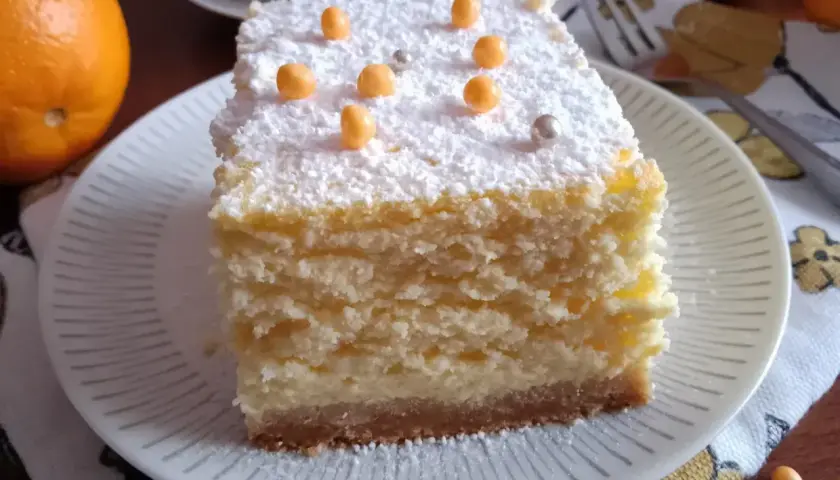 Pyszny sernik pieczony z delikatnym spodem z herbatników, posypany cukrem pudrem i pomarańczowymi kuleczkami.