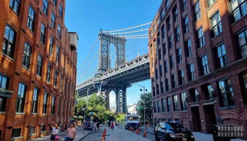Ulica w **brooklyn** z ceglanymi kamienicami i majestatycznym mostem w tle.