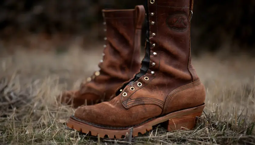 Two brown leather work boots with a lug sole, meaning a thick, rugged sole with deep treads for excellent grip, stand in dry grass.