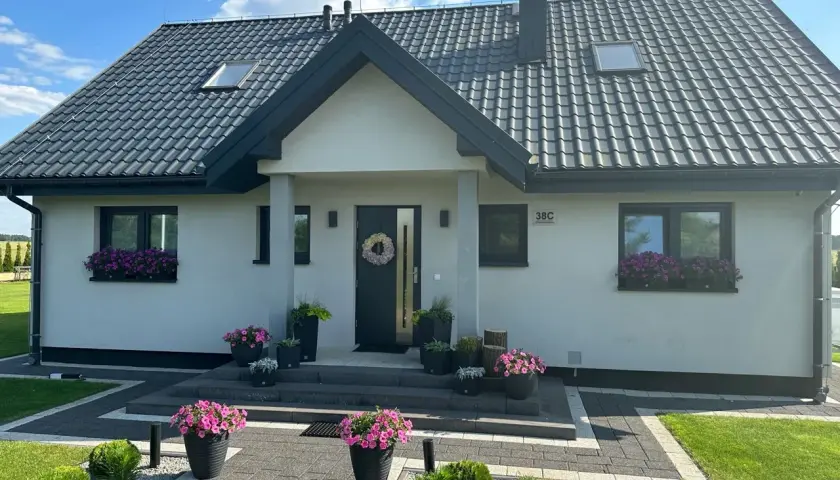 Uroczy dom Kamilek 100m2 z kwitnącymi petuniami w donicach i skrzynkach, zadbany ogród, nowoczesna elewacja.