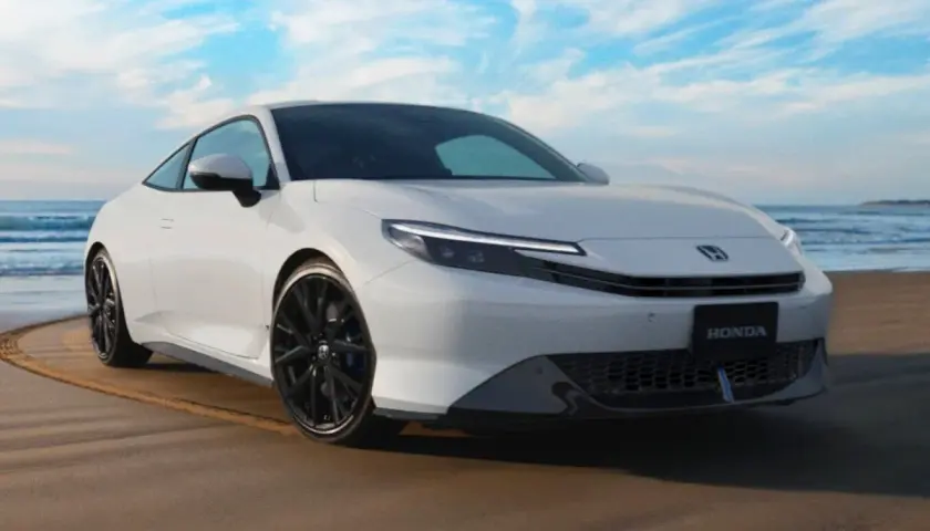 El Honda Prelude 2026 blanco, con su diseño deportivo, se luce en la playa bajo un cielo azul.