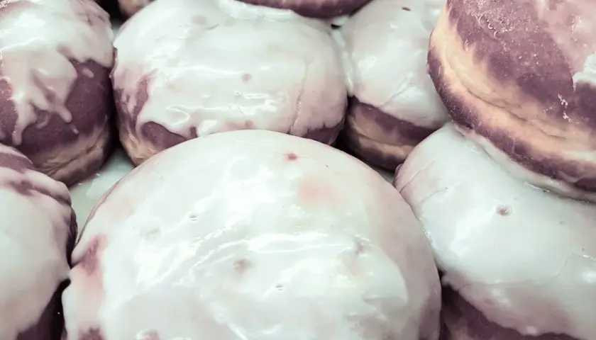 Pączki z fioletowym nadzieniem, polane błyszczącym lukrem z cukru pudru, kuszą swoim wyglądem.