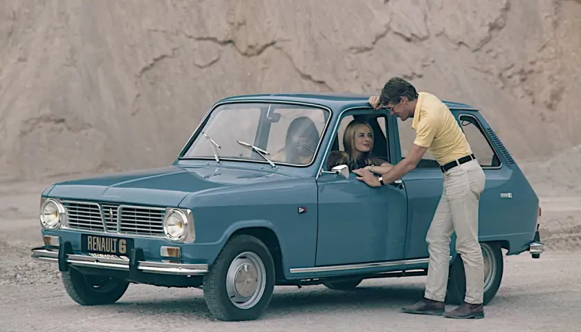 En man lutar sig mot en blå Renault 6, en av många gamla Renault-modeller, medan en kvinna sitter bakom ratten.