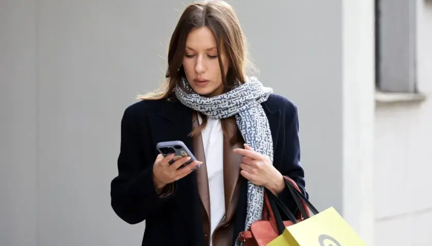 Kobieta w granatowym płaszczu i wzorzystym szaliku trzyma telefon. Czyżby szukała informacji, jaki kolor jest teraz modny?