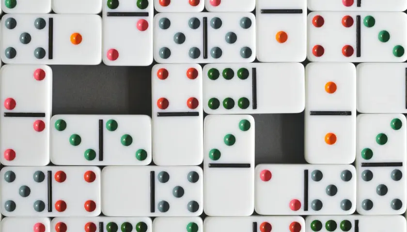 Wiele białych kostek domino z kolorowymi kropkami, tworzących wzór. Ile kostek domino?